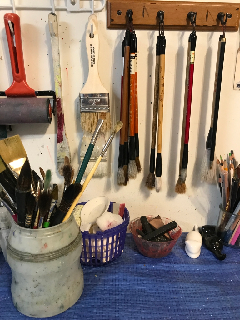 Painters brushes hang on hooks on the wall.